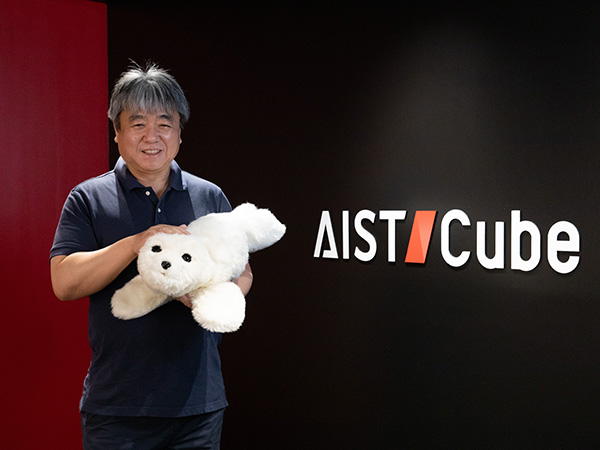 AIST-Cubeの看板の前でパロを抱く柴田さん