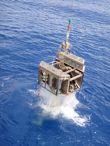 海から引き上げられるグラブ採泥器の写真